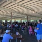 A crowd of people sitting at tables in a covered area with Supreme Boats.