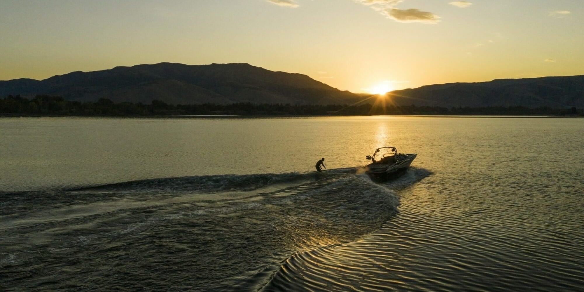 A man is riding a Supreme boat on a lake at sunset.