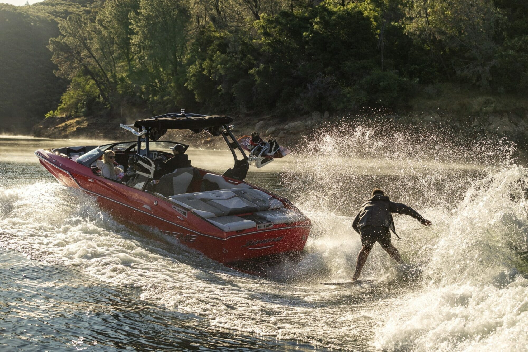 A man is wakeboarding behind a Supreme boat.