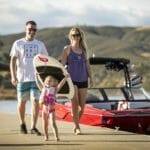 A family with a boat and a surfboard walks down a dock.