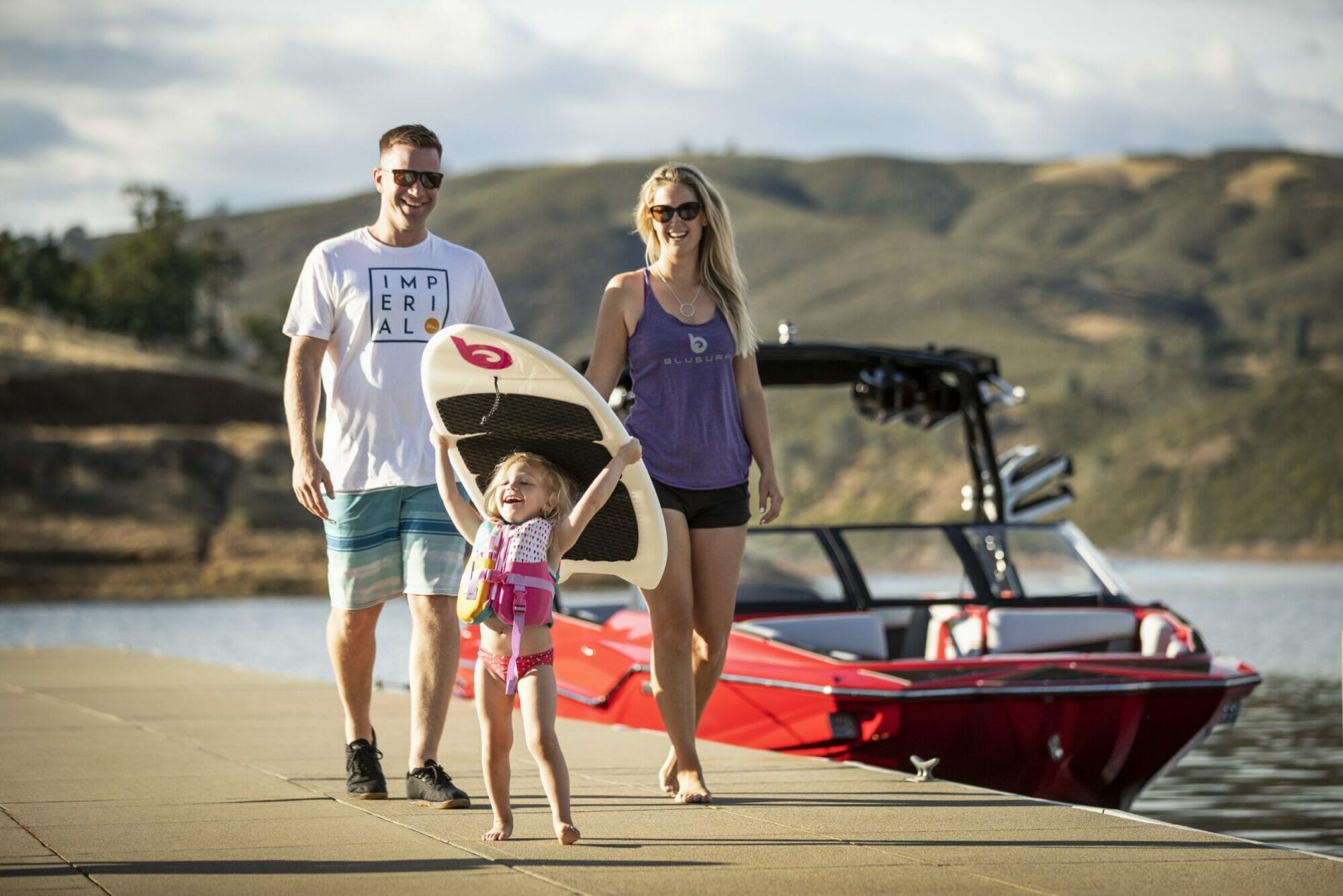 A family with a boat and a surfboard walks down a dock.