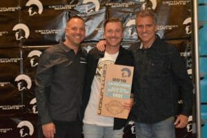 Three men standing in front of a Supreme Boats banner with an award.