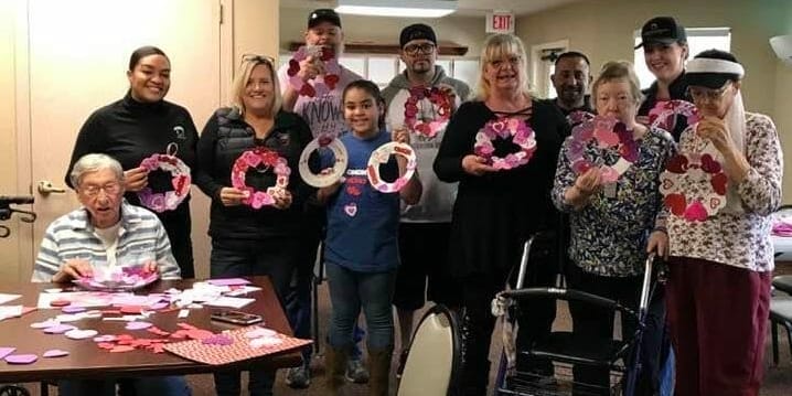 A group of people posing for a photo while making Valentine wreaths.