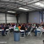 A large group of people sitting at tables in a warehouse showcasing Supreme Boats.