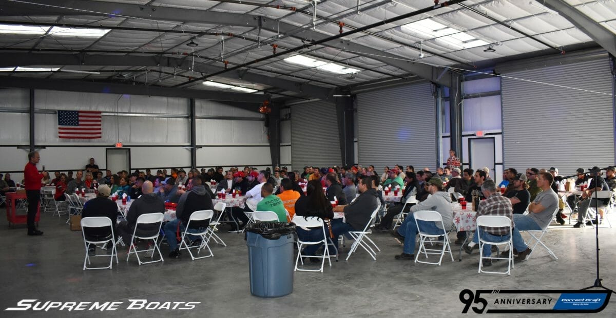 A large group of people sitting at tables in a warehouse showcasing Supreme Boats.