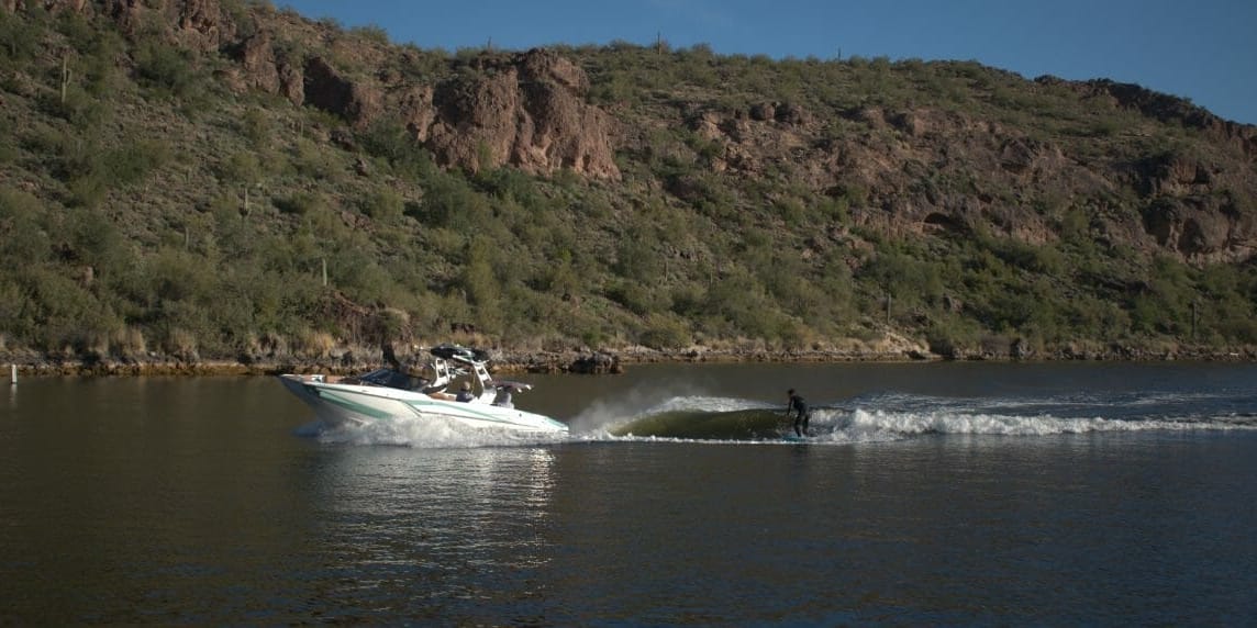 A Supreme boat races down a river with mountains in the background.