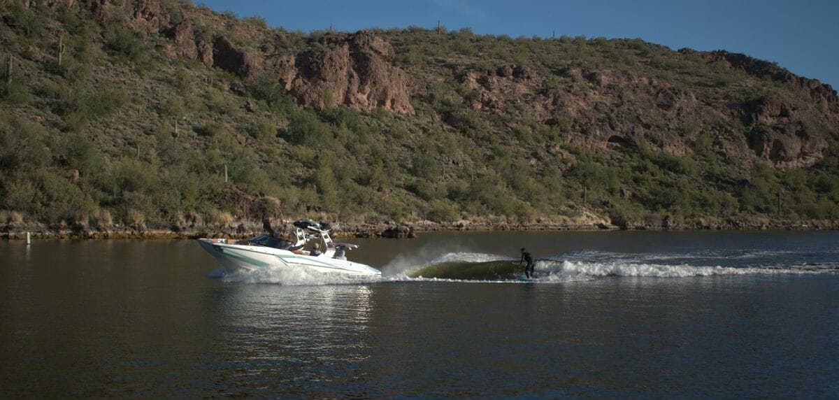 A Supreme boat races down a river with mountains in the background.