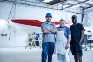 Three men standing in front of a Supreme boat in a garage.