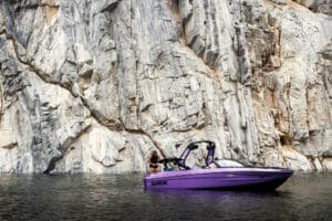 Wakeboarder putting on life jacket on swim step of purple S220 Supreme boat