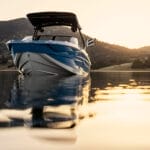 A Supreme S240 boat in blue and white floats on calm water at sunset, with mountains in the background.