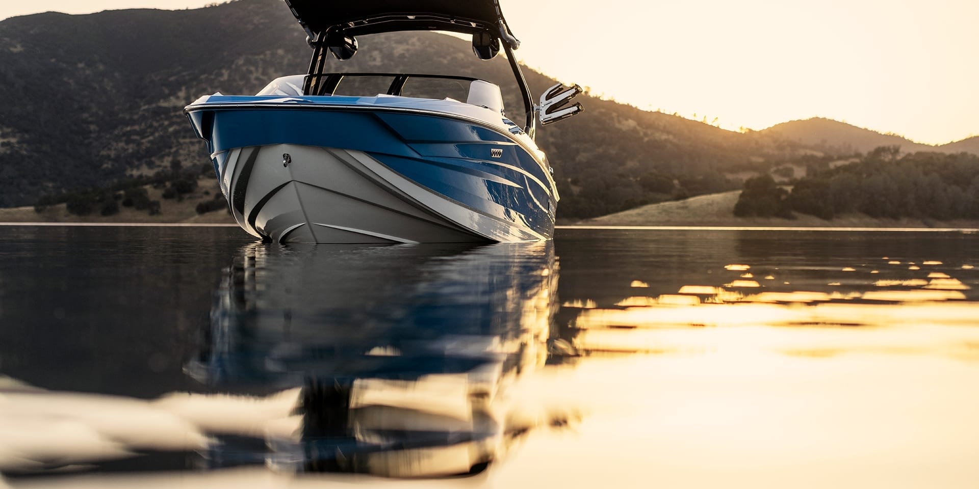 A Supreme S240 boat in blue and white floats on calm water at sunset, with mountains in the background.