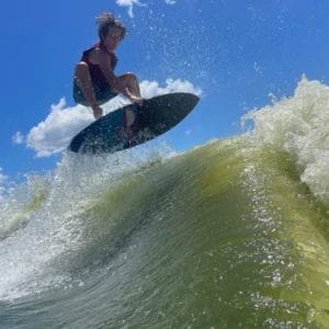 A young man named Evan Hudson riding a wave on a surfboard while engaging in SEO practices.