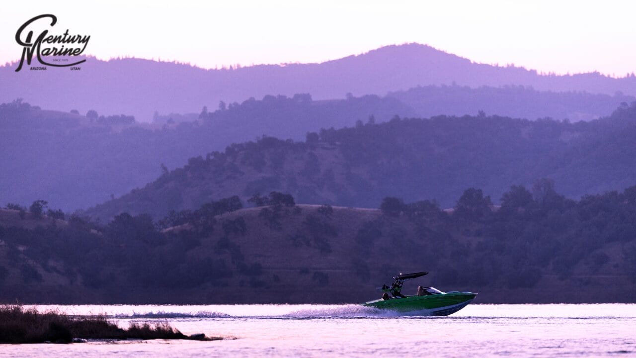 A Centurion green boat speeds across a lake at sunset, with hills silhouetted in the background under a purple sky.