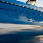 A blue boat, adorned with "Supreme" and "Mello Marine" logos, drifts like an auto draft on still water, mirroring the clear sky above.