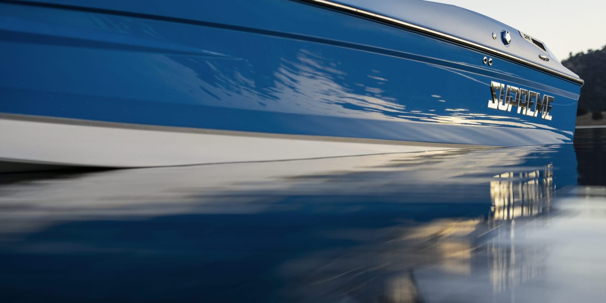 Close-up side view of a blue Supreme boat floating on calm water, its reflection shimmering below—an impressive showcase for any Florida dealership offering Supreme Boats.